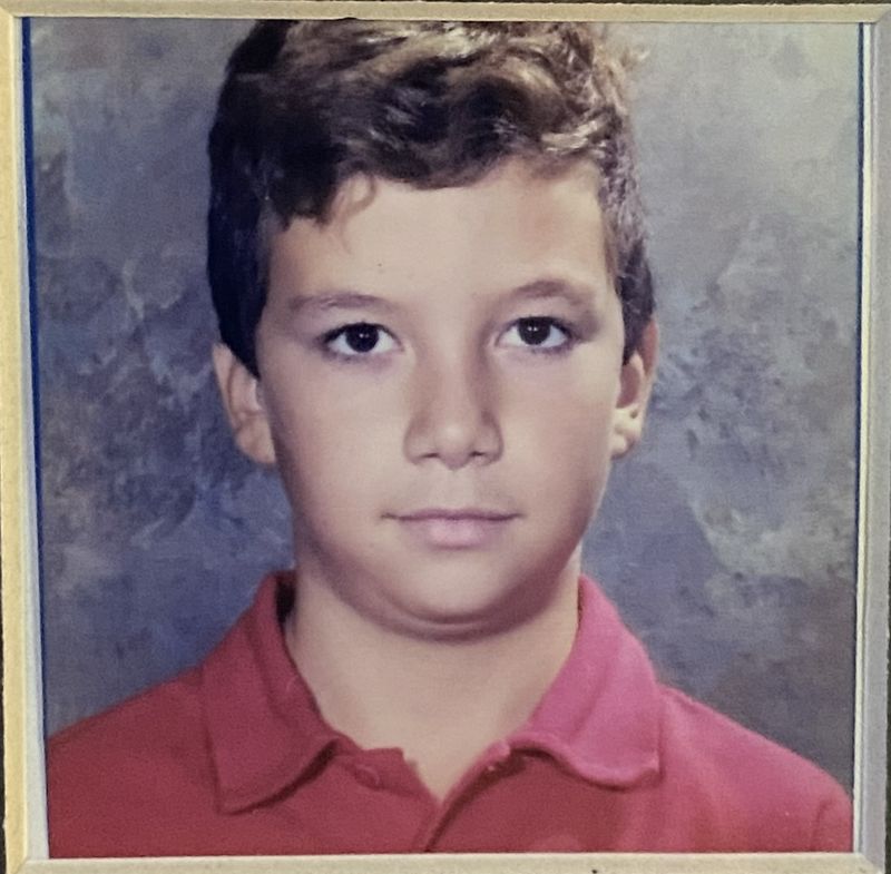 Foto de carnet de Eftim de niño, con polo rojo, sobre fondo azul jaspeado